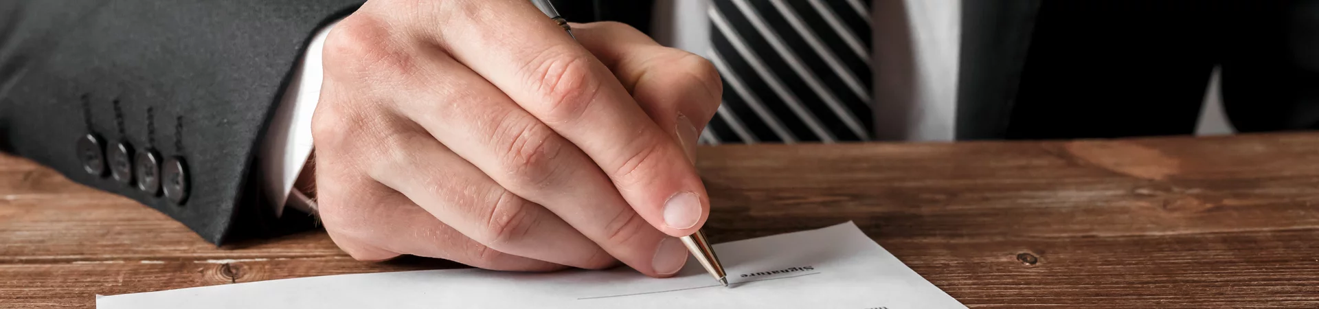 A suited man is engaged in signing a document on a table