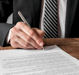 A man in a suit is signing a document on a table, indicating a formal agreement. A man in a suit is signing a document on a table, indicating a formal agreement.
